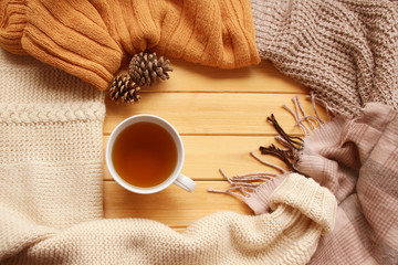 cup of hot fragrant tea on a wooden background, autumn leaves, apple, cozy scarves and knitted sweaters, flat, concept hugge, winter or autumn mood, copy space