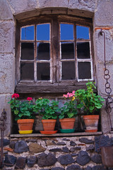 Fototapeta na wymiar An old window frame decorated with potted Geraniums in Normandy France