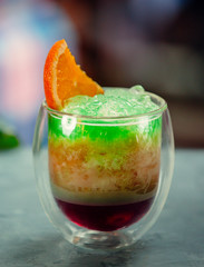 A glass of exotic juice with green ice shaving and orange slice on top