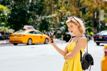 Woman with cell phone waiting in front of a yellow cab in New York