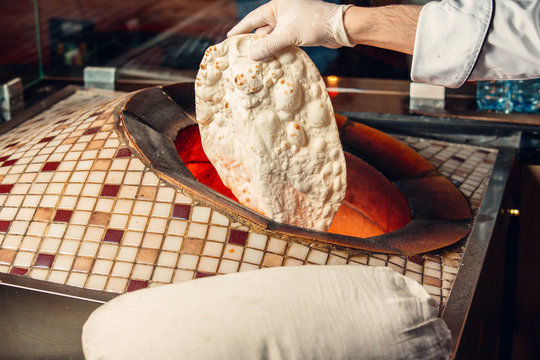 Men putting lavash pita flatbread into special oven tandoor