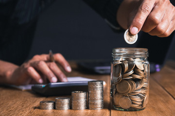 Men are Saint documents about save money and put coin in glass jar on desk on black background.