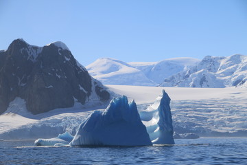 wystający ponad taflę wody wierzchołek góry lodowej przy wybrzeżu antarktydy w słoneczny dzień - obrazy, fototapety, plakaty