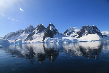 spokojne zimne wody pomiędzy ośnieżonych skałami u wybrzeży antarktydy w piękny słoneczny dzień - 292354309