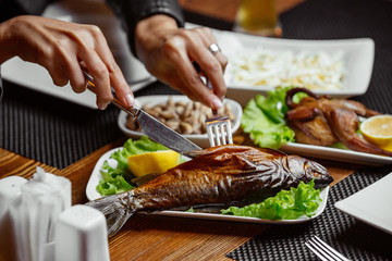 Woman cutting dried smoked fish served with lettuce leaves and lemon