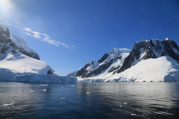 spokojne zimne wody pomiędzy ośnieżonych skałami u wybrzeży antarktydy w piękny słoneczny dzień - obrazy, fototapety, plakaty