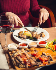 Woman cutting grilled chicken steak served with grilled peppers, salad and wine