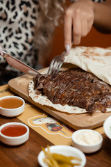 Woman cutting lamb steak on flatbread served with mayo and ketchup