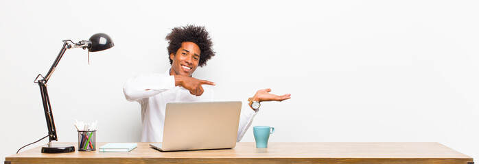 young black businessman smiling, feeling happy, carefree and satisfied, pointing to concept or idea...