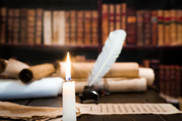 A lit candle against the background of blurred scrolls, books and bird feathers
