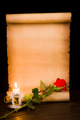 A scroll of parchment, a red rose and a lit candle
