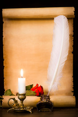 A scroll of parchment, a red rose, a feather and a lit candle