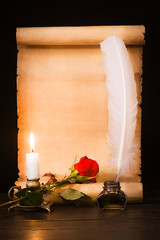 Scroll of old parchment, red rose, feather and lighted candle