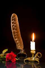 Red rose, feather in the inkwell and candle in the candlestick on a black background