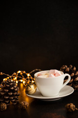Warm cocoa drink with marshmallows. Christmas and New Year drink. Christmas Eve mood. Christmas lights and decorations. Winter holidays concept. Dark background. Vertical. Copyspace