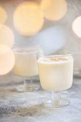 Eggnog traditional homemade Christmas and New Year drink with cinnamon and nutmeg. Winter holidays mood. Christmas lights. Light background. Selective focus. Vertical