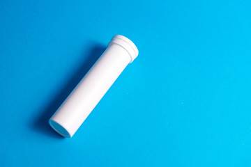 Round white matte aluminum tube with cap for effervescent or carbon tablets, pills, vitamins. Side view. New sealed vertical tube to store medicine lying isolate on blue background. copy space