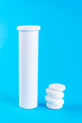 Round white matte aluminum tube with cap for effervescent or carbon tablets, pills, vitamins. Side view. Laying open the tube and next to a stack of drugs. isolated on blue background. copy space