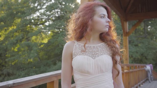 Elegant caucasian woman with red hair stands on the bridge in the autumn park. Natural delicate beauty of a young readhead girl.
