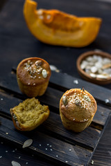 Pumpkin muffins on a dark wooden and half a broken cupcake and a slice of pumpkin in the background and seeds