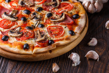 Pizza with tomato, olives, champignons, ham and cheese on round wooden plate
