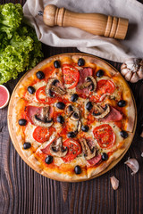Pizza with tomato, olives, champignons, ham and cheese on round wooden plate