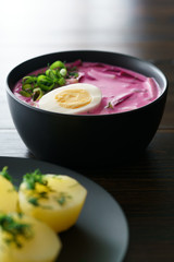 Lithuanian Saltibarsciai (Cold Beet Soup) with hard boiled egg and potatoes, seasoned with spring onions and dill. Dark wooden table, high resolution
