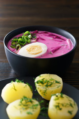 Lithuanian Saltibarsciai (Cold Beet Soup) with hard boiled egg and potatoes, seasoned with spring onions and dill. Dark wooden table, high resolution