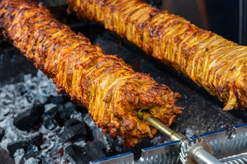 A rotating spit roast of meat over hot coals as used to make kebabs at a street food vendor stall.
