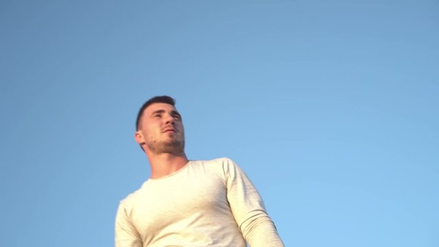 Portrait of a young guy on a background of clear blue sky. Close-up of a guy wearing a gray longsleeve looking to the side.