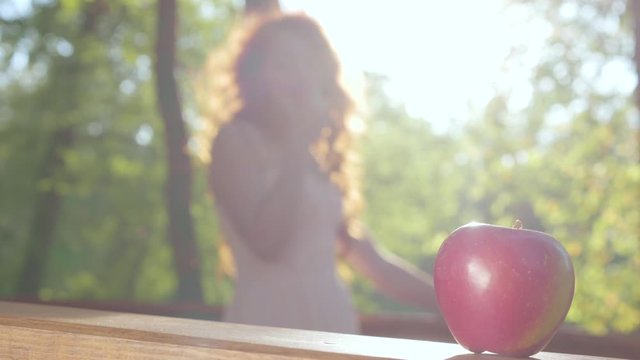 Close-up of a red apple with a redhead caucasian woman in the sunshine at the background. Snow White style. Fairy forest.