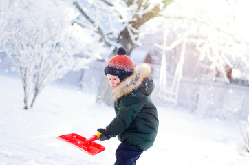 Boy playing in the snow with a red shovel. Winter fun walk.