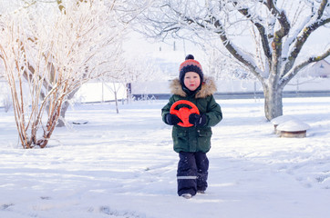 Fototapeta na wymiar A boy in a bright orange hat walks through the snowy winter Park