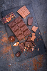 Pieces of dark and milk chocolate and cocoa on a dark background, top view.