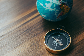 One gold compass on top of a wooden desk next to a model of an earth globe
