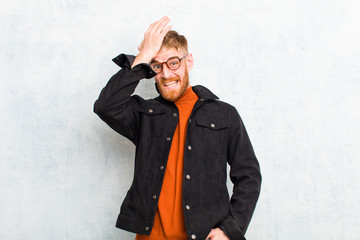 young red head man raising palm to forehead thinking oops, after making a stupid mistake or...
