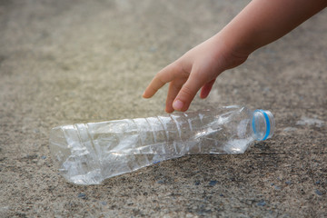 Kid hand picking up a waste plastic drinking bottle 