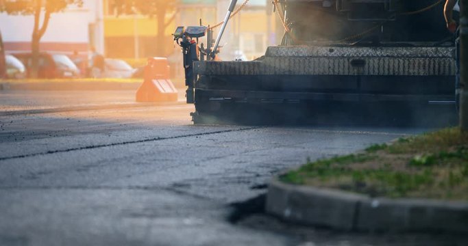 Workers change the asphalt repair the road surface. Work on new road construction site. Team of workers put hot asphalt on a street. Steam rising from hot asphalt surface. Asphalt road construction.