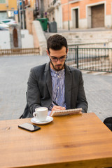 Young businessman is writing in his notebook in a bar terrace