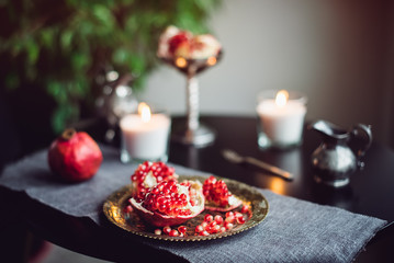 Obraz na płótnie Canvas Still life composition with juicy red cut cleared pomegranate on a copper plate, burning candles and other oriental decor on the black table. Soft selective focus. Copy space.