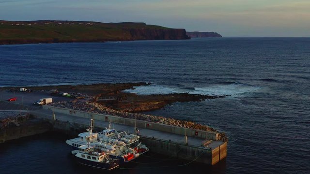 Aerial of boats docked in Doolin pier and Cliffs of Moher at sunset