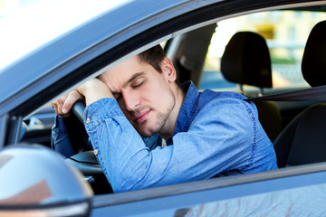 Man fell asleep behind steering wheel of car. Sleepy driver is riding in automobile. Male is...