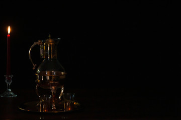 Vintage brass coffee warmer next to candle on left side of black background