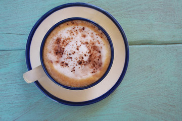 Top view of hot coffee  cappuccino cup or hot drink cocoa with milk foam and cinnamon powder on light blue pastel painted wood table background.