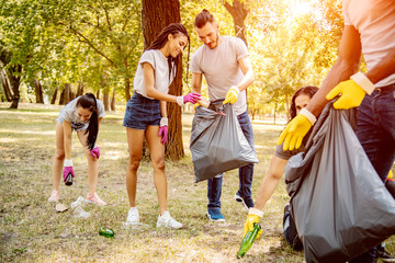 Team of friends cleaning up the park by collecting litter into plastic bags