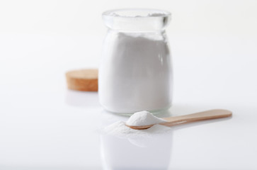 Baking soda in a jar and a wooden spoon on a white glossy table