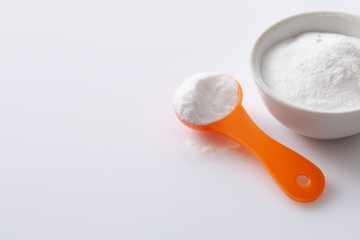 Measuring spoon with artificial sweetener aspartame E951 and a bowl of blemish on a white glossy background