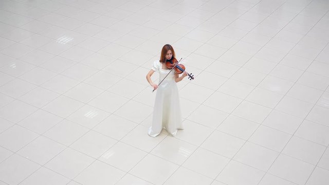 Lady in a white dress is standing on white tile and playing the violin
