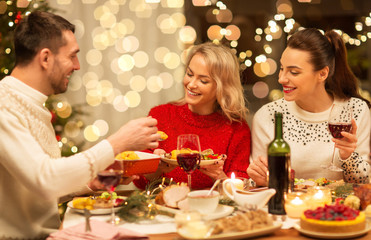 holidays and celebration concept - happy friends having christmas dinner at home, eating and drinking