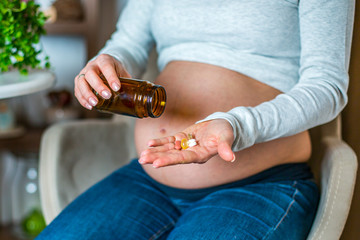 Young beautiful pregnant girl taking medication in her home during daytime